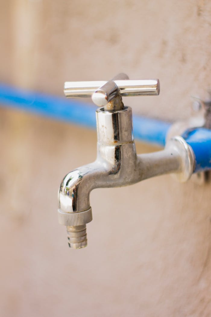 who-we-are A close-up view of a shiny stainless steel faucet attached to a blue pipe on a wall.