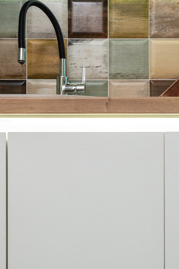 Stylish kitchen sink featuring a sleek black faucet and vibrant multicolored backsplash tiles.